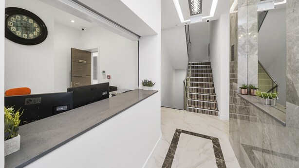 Un área de recepción moderna con mostrador de recepción, un reloj y una escalera que conduce a un nivel superior.