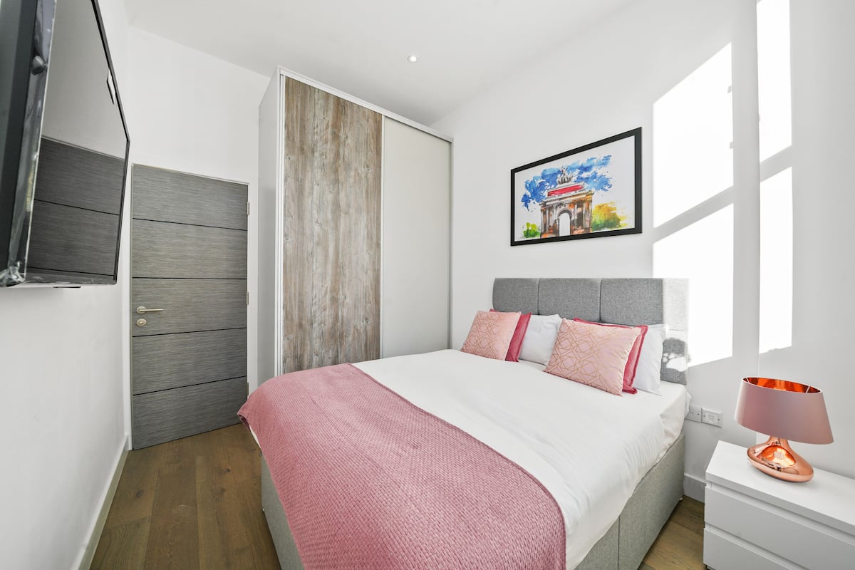 A bedroom with a bed, a nightstand, a lamp, a wardrobe, and a painting on the wall.