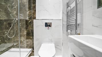 Et moderne badeværelse med en glasvæg omkring brusebad, et hvidt toilet og et fritstående badekar.