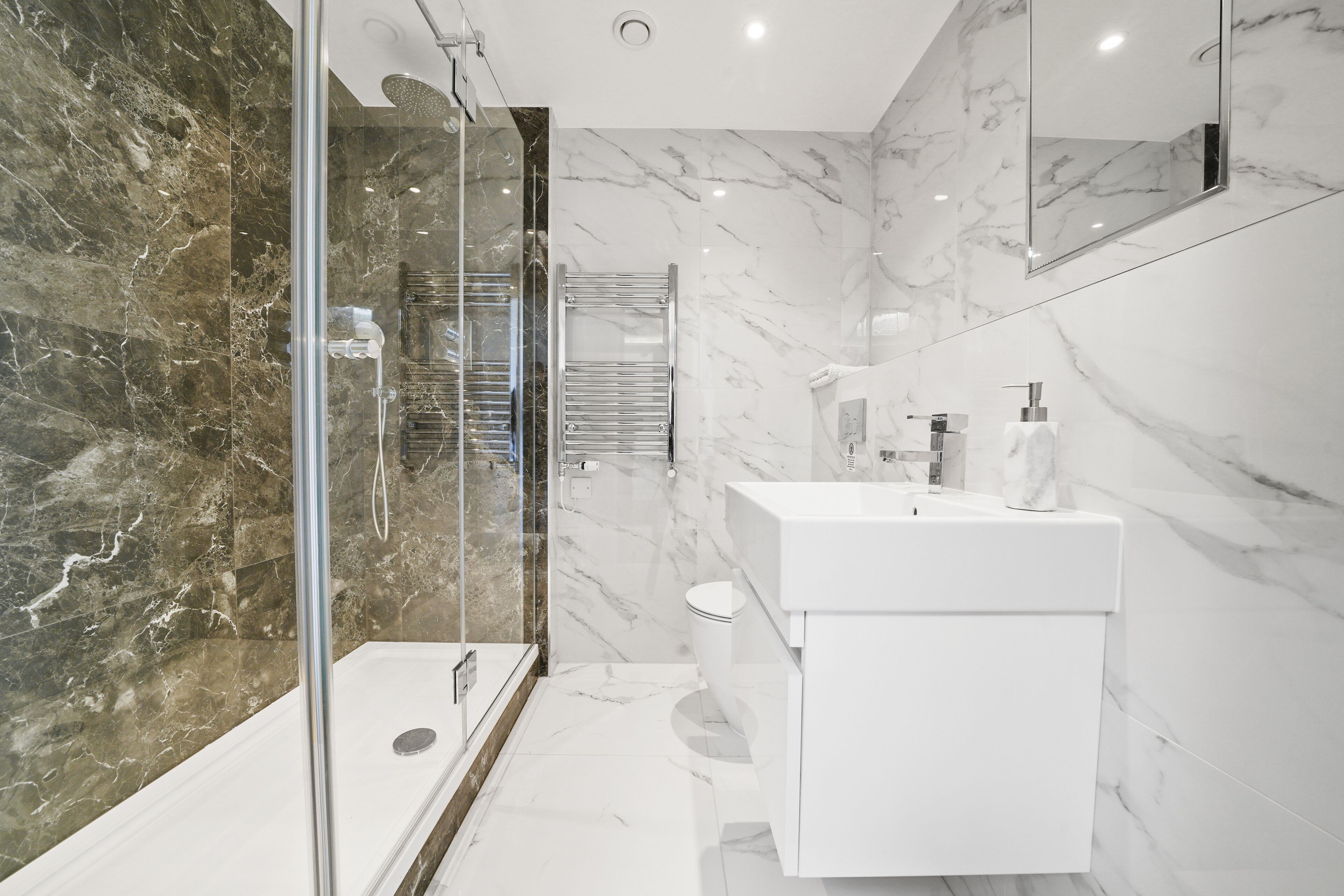A modern bathroom with a glass shower enclosure, a white sink, and marble walls.