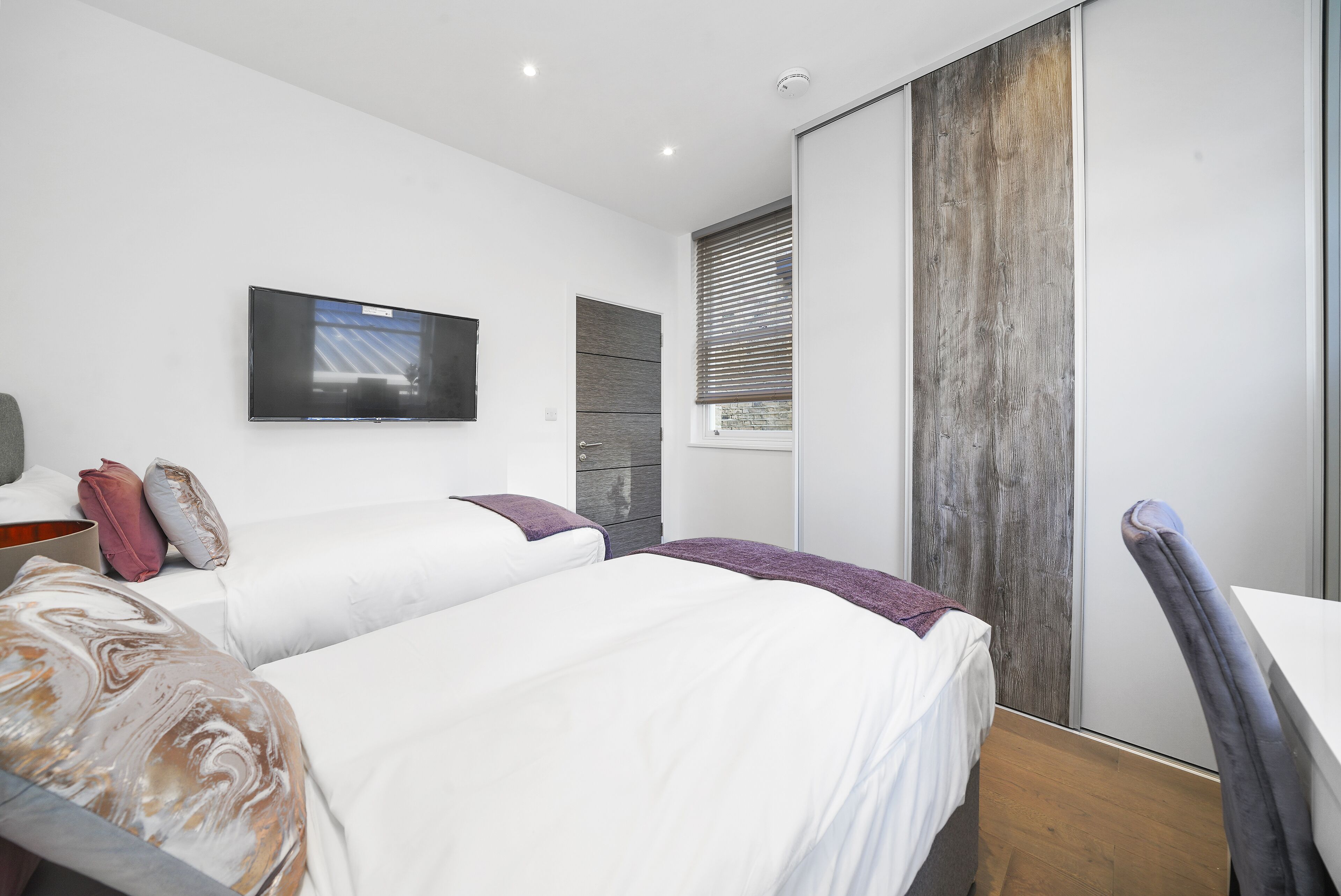 A modern bedroom with a large bed, a flat-screen TV mounted on the wall, and a sliding door with a wooden finish.