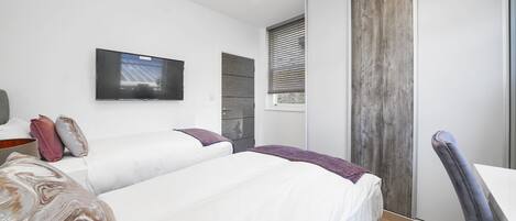 A modern bedroom with a large bed, a flat-screen TV mounted on the wall, and a sliding door with a wooden finish.