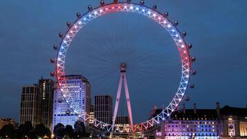 A large Ferris wheel with a red and white light pattern, surrounded by buildings and a river.