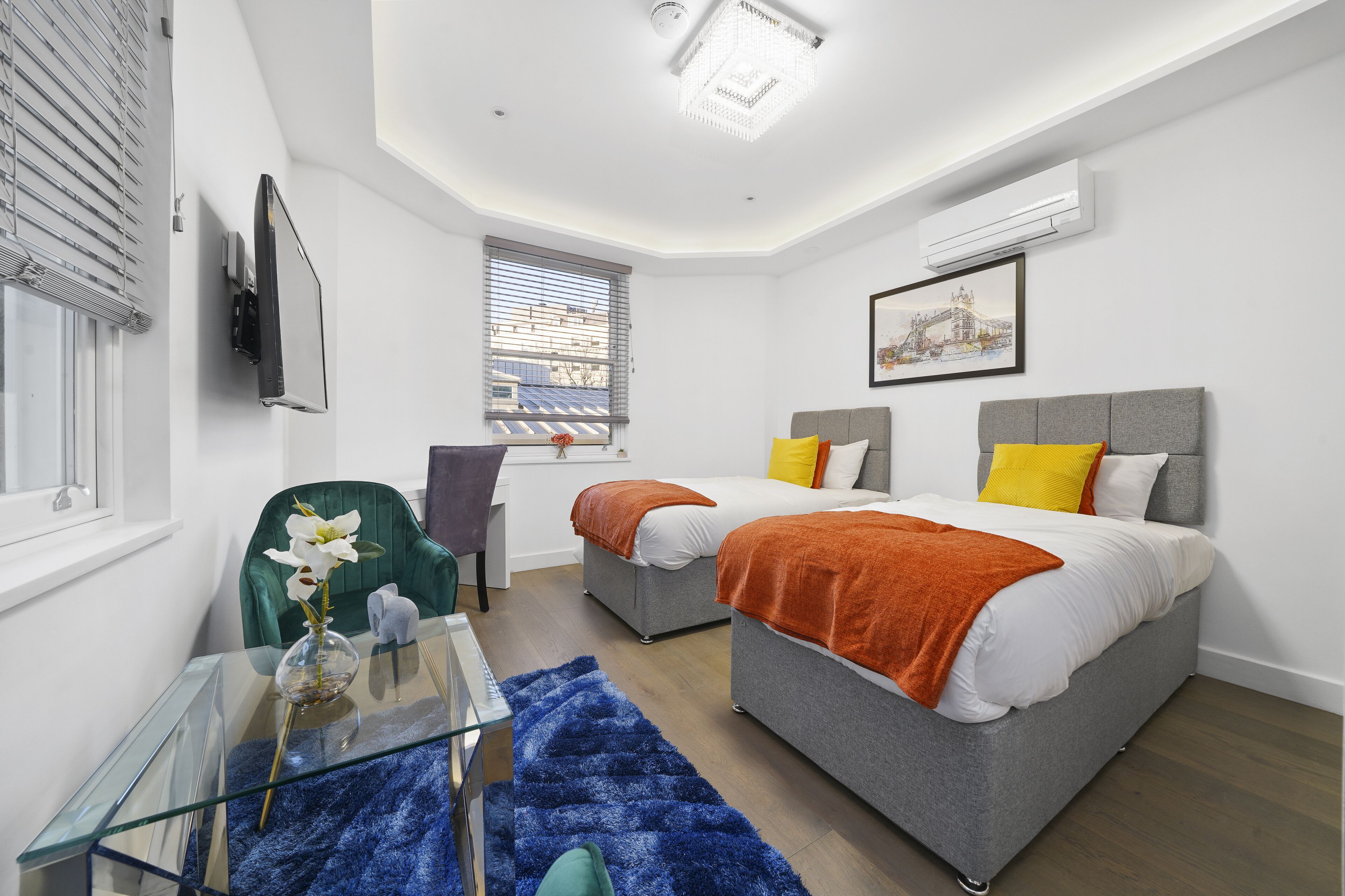 Une chambre moderne avec deux lits, une table en verre, une chaise et une fenêtre avec des stores.