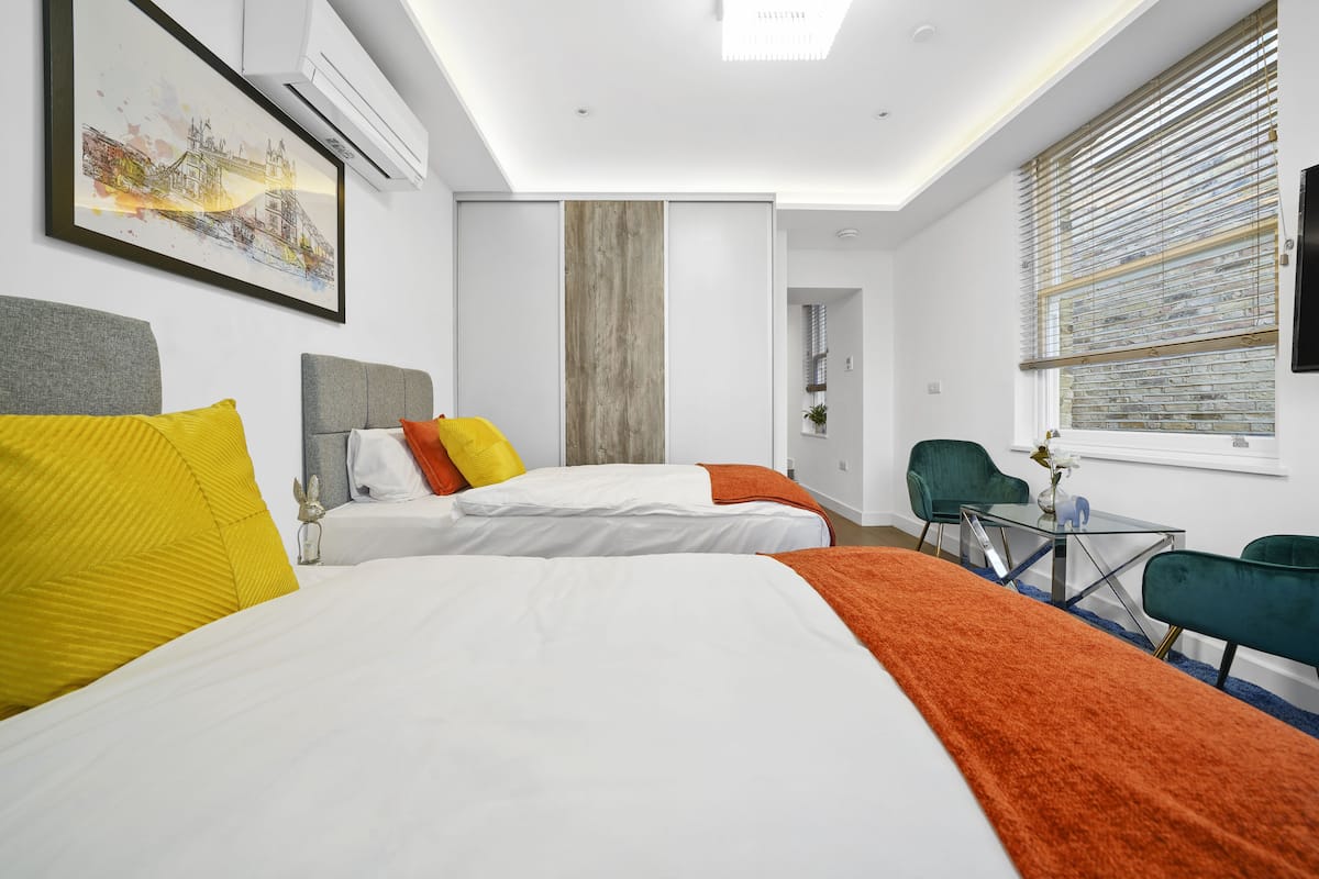 A hotel room with two beds, a desk, and a window with blinds.