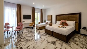 A hotel room with a large bed, two smaller beds, a TV, a desk with a chair, and a marble floor. - Grand Hotel Serapide (Pozzuoli)