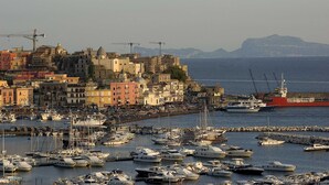 A marina with numerous boats docked, a red ship, and colorful buildings in the background. - Grand Hotel Serapide (Pozzuoli)