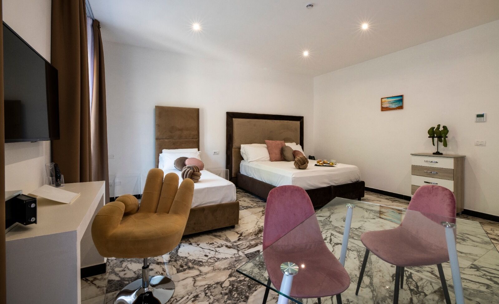 Habitación de hotel con cama, dos sillas, escritorio, televisor y una pequeña planta.