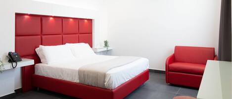 Una habitación de hotel moderna con una cama roja, un sofá rojo y una mesita con un teléfono.