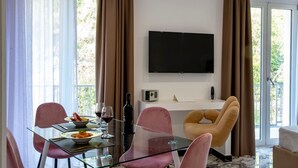 A modern dining area with a glass table, pink chairs, and a TV mounted on the wall. - Grand Hotel Serapide (Pozzuoli)