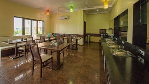A restaurant with multiple dining tables and chairs, a buffet counter, and a large window providing natural light.