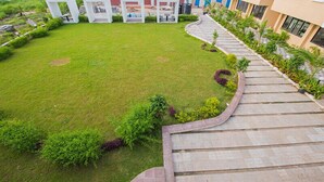 A courtyard with a grassy lawn, white geometric planters, and a curved stone pathway leading to a building with multiple windows.