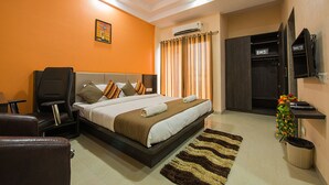 A hotel room with a bed, a desk, a chair, a TV, and an air conditioning unit.