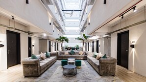 Een ruime lobby met een hoge plafond, een centraal zithoek met sofa’s en ronde tafels, en uitzicht op een trap die naar een hoger niveau leidt.
