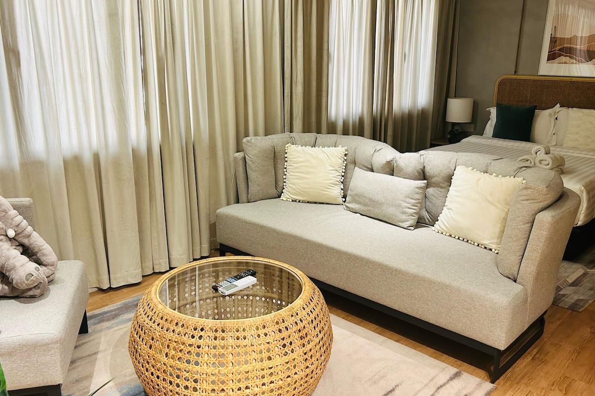 A bedroom with a sofa, a bed, a wicker ottoman, and a stuffed elephant toy.