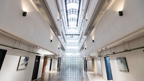 Ruim, modern interieur met een hoge plafond en dakramen, met een centrale trap en kunstwerken op de muren.