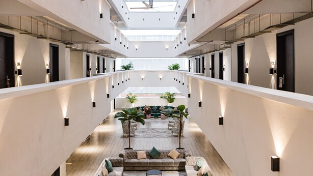Een ruime hotellobby met een centraal zitgedeelte, meerdere deuren en een hoge plafond met dakramen.