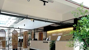 Een receptiezone met een receptiebalie met de tekst 'URBAN LIVING RECEPTION', een modern design met een houten vloer en een groot raam dat natuurlijk licht binnenlaat.