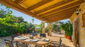 An outdoor patio with a wooden pergola, a round table set for dining, and potted plants around. - SA ROTA Finca for 6 people in Ariany with pool (Ariany)