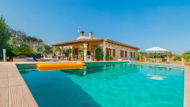 A pool area with a wooden deck, lounge chairs, and a building with a tiled roof. - SA ROTA Finca for 6 people in Ariany with pool (Ariany)