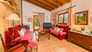 A cozy living room with a fireplace, red sofas, a television, and a wooden ceiling. - SA ROTA Finca for 6 people in Ariany with pool (Ariany)