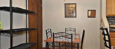 Un comedor con una mesa y sillas, una estantería metálica, un armario de madera y una araña.