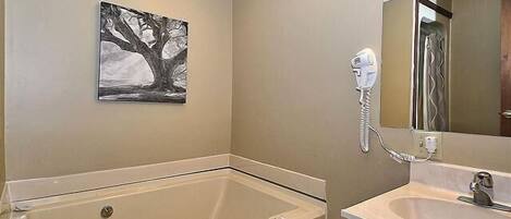 Un baño con bañera, lavamanos, secador de pelo y un cuadro en la pared.