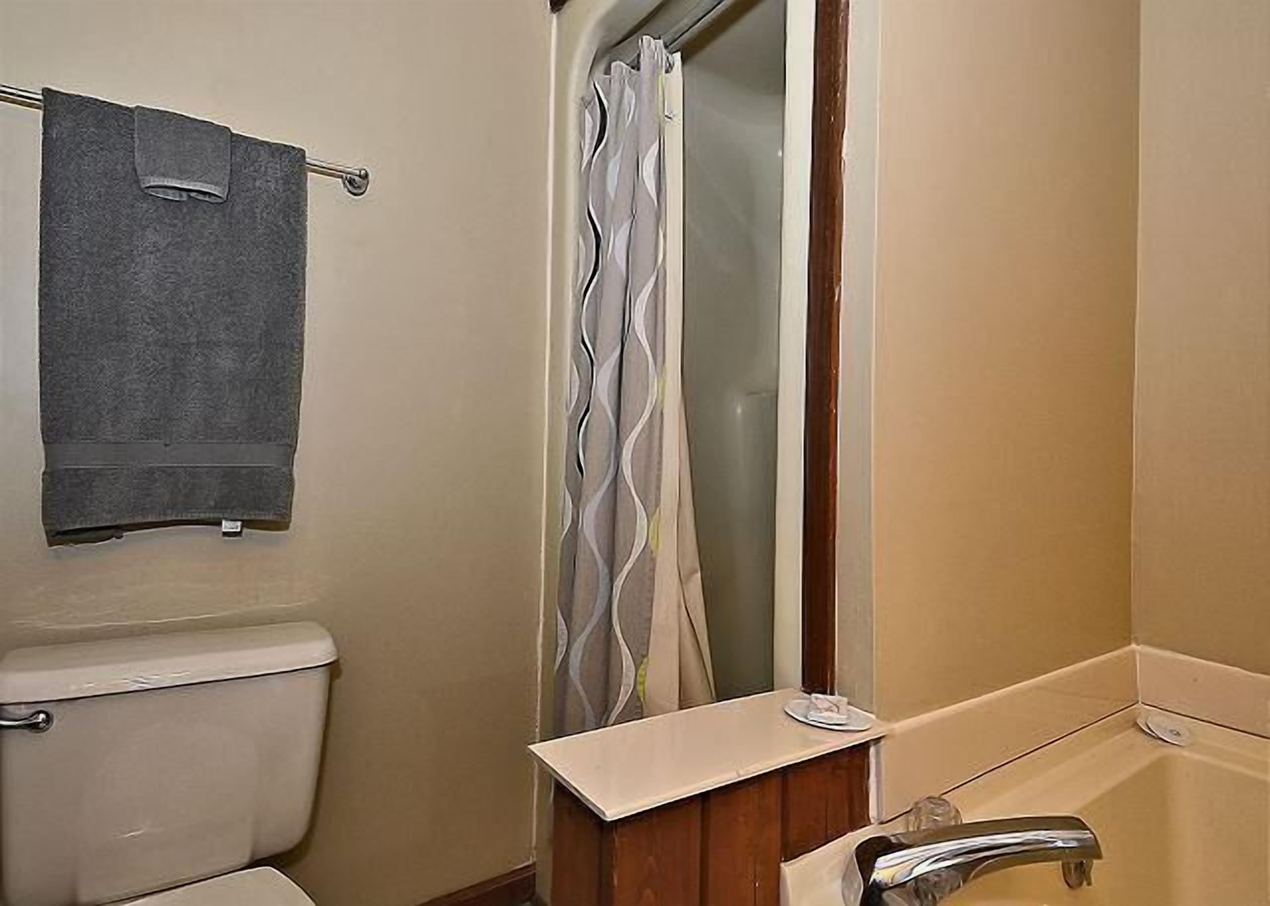 A bathroom with a toilet, a towel rack with a towel, a shower curtain, and a bathtub.
