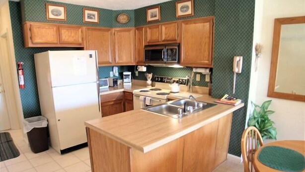 A compact kitchen with wooden cabinets, a refrigerator, a microwave, and a sink.