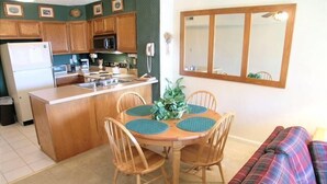 A compact kitchen with wooden cabinets, a refrigerator, and a dining area with a table and chairs.