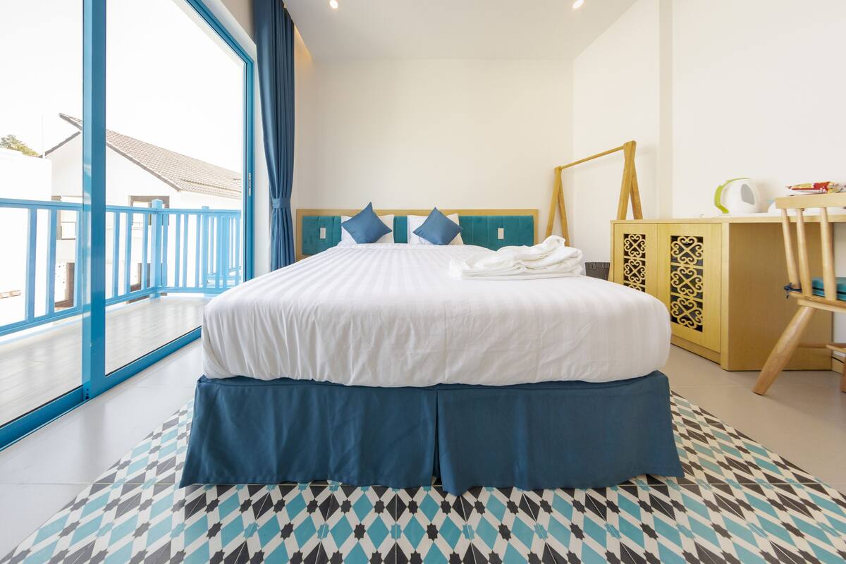 A hotel room with a large bed, a view of the balcony, and a patterned floor.