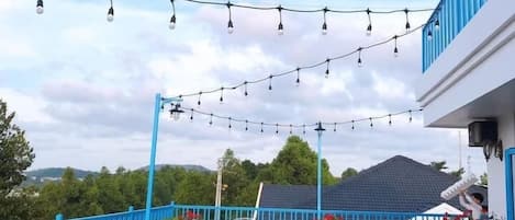 An outdoor patio area with tables and chairs, string lights, and a blue railing.