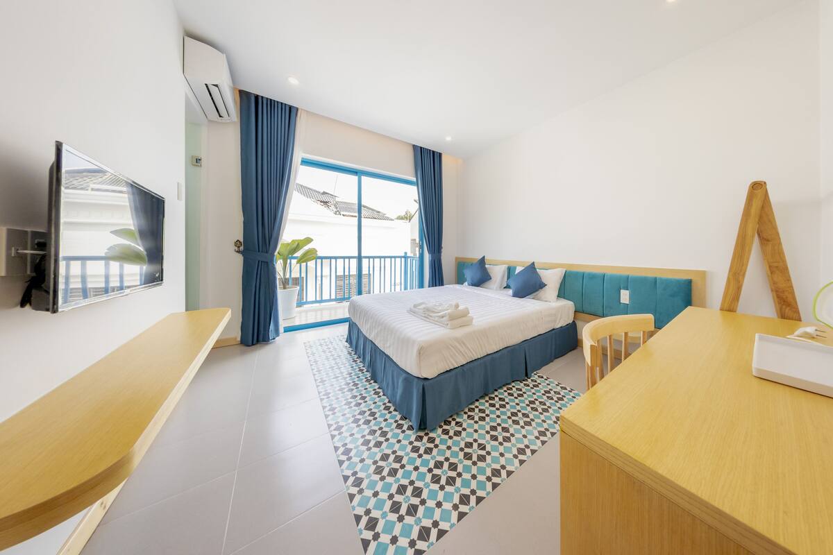 A modern hotel room with a large bed, a desk, and a balcony with a view.