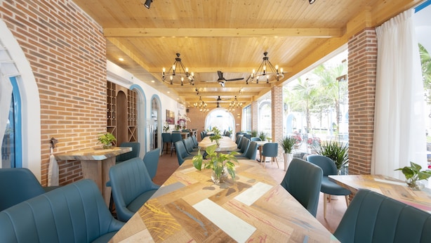 A spacious indoor dining area with a long wooden table, blue upholstered chairs, and a brick wall. - TURI STAYpoint (Nghia Lo)