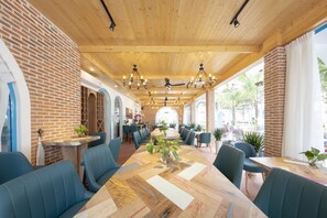 A spacious indoor dining area with a long wooden table, blue upholstered chairs, and a brick wall. - TURI STAYpoint (Nghia Lo)