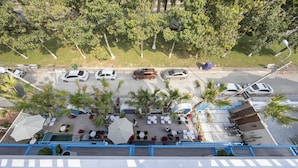 An aerial view of a parking area with several cars, palm trees, and outdoor seating with umbrellas. - TURI STAYpoint (Nghia Lo)