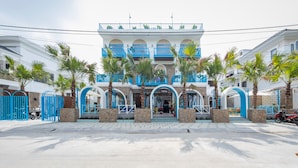 A two-story building with a white facade and blue accents, featuring a central entrance with a staircase and palm trees. - TURI STAYpoint (Nghia Lo)