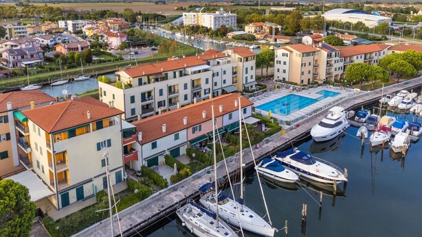 A marina with boats docked, surrounded by residential buildings with balconies and a swimming pool.