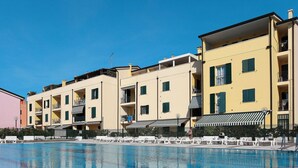 A swimming pool with white lounge chairs and a row of yellow buildings with balconies.