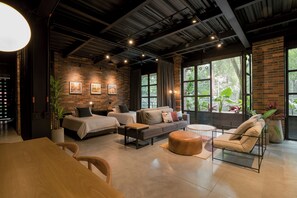 A modern hotel room with a brick wall, large windows, a sofa, a dining table, and a small round table. - Fantastic 2BR Apt in the heart of Provenza (Medellín)