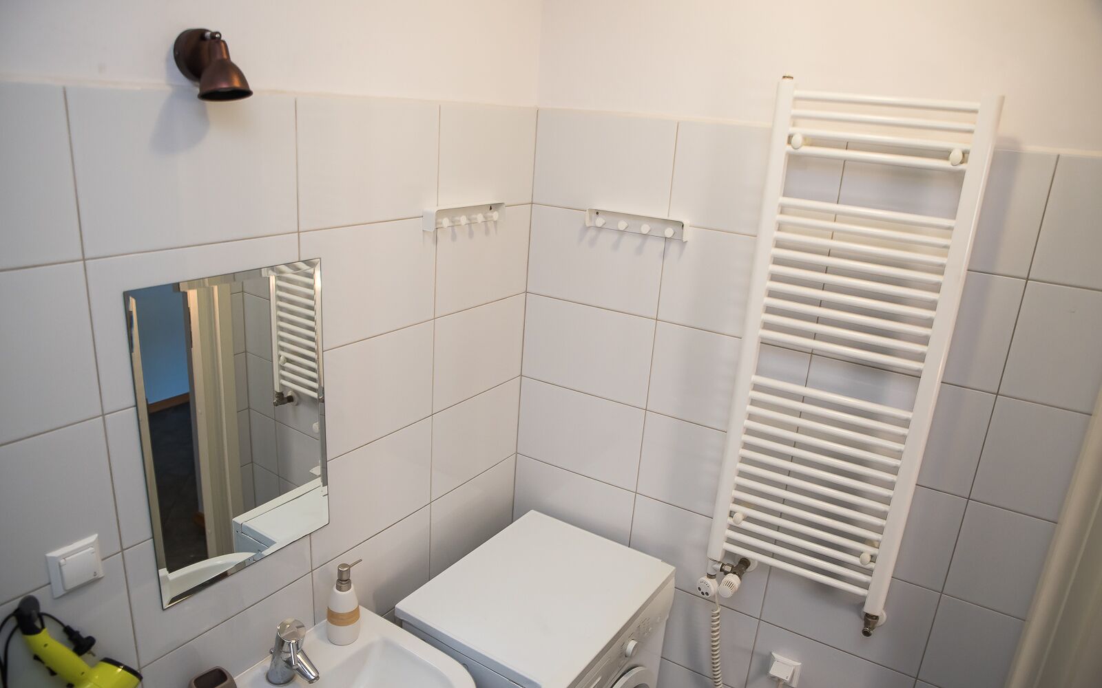 A bathroom with white tiles, a sink, a mirror, a towel rack, and a white radiator.