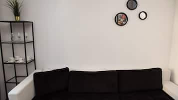 A modern living room with a black sofa, a white armchair, and a black shelving unit with decorative items.