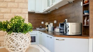 Une cuisine avec des meubles blancs, un four à micro-ondes et un panier en osier contenant des plantes vertes.