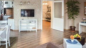 Un salon moderne avec un mur en briques, un téléviseur à écran plat, un coin repas avec une table et des chaises, et une grande plante en pot.