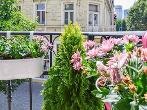 A balcony with potted plants and flowers, a railing, and a building in the background.