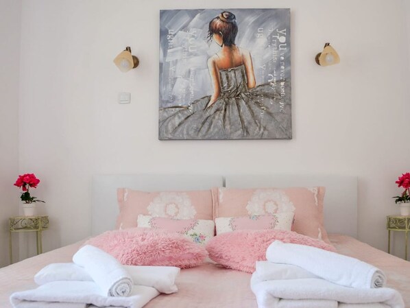 A bedroom with a bed, pillows, a painting, and two bedside tables with flowers.