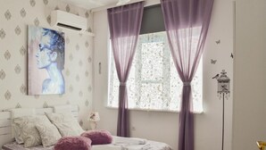 Une chambre à coucher comprenant un lit, une table de chevet, un climatiseur fixé au mur, une fenêtre avec des rideaux violets et une lampe sur pied.