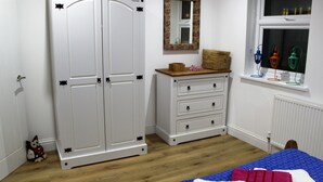 Un dormitorio con armario doble, cómoda, espejo, ventana decorada y cama con colcha azul y roja.