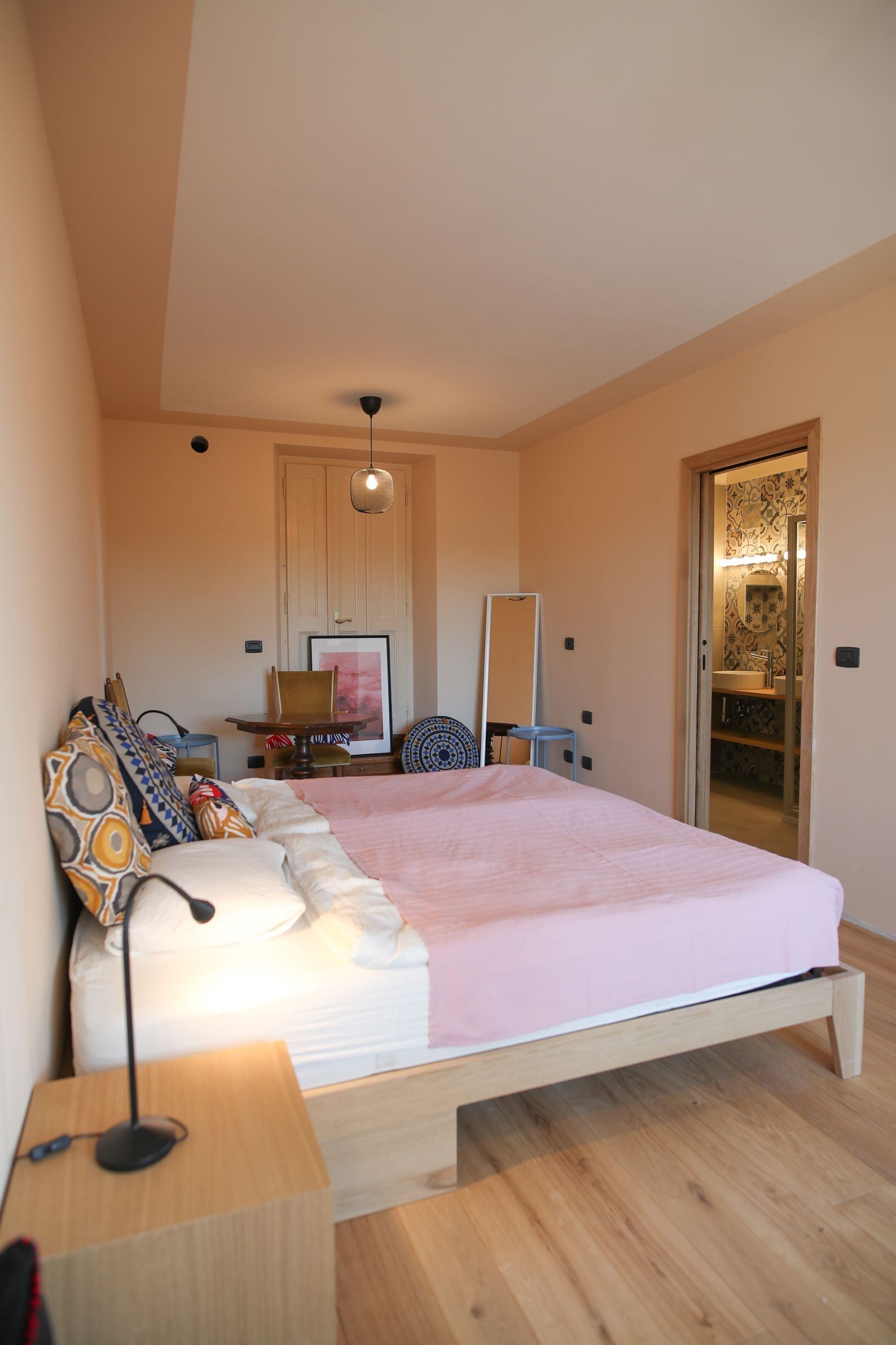 Une chambre à coucher comprenant un lit, une table de chevet, une lampe et une porte donnant sur une salle de bain.