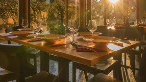 A dining area with a table set for two, large windows, and a view of trees and buildings. - Casa Vinitoscani (Perroy)